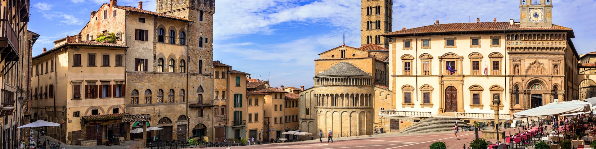 A historic square with a prominent tower, a church with a bell tower, and a café area.
