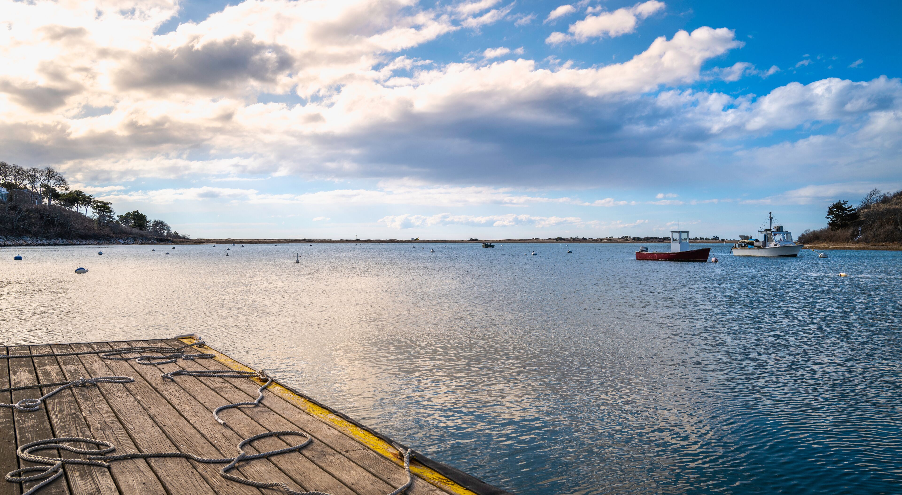 Sunrise over the dock with scattered ropes and trawlers moored in the bay in Harwich harbor in Massachusetts. Dramatic cloudscape over the Atlantic Ocean at dawn.