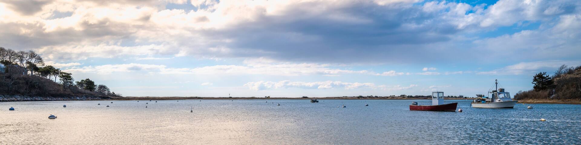 A calm lake with a wooden dock and a red boat anchored in the distance.