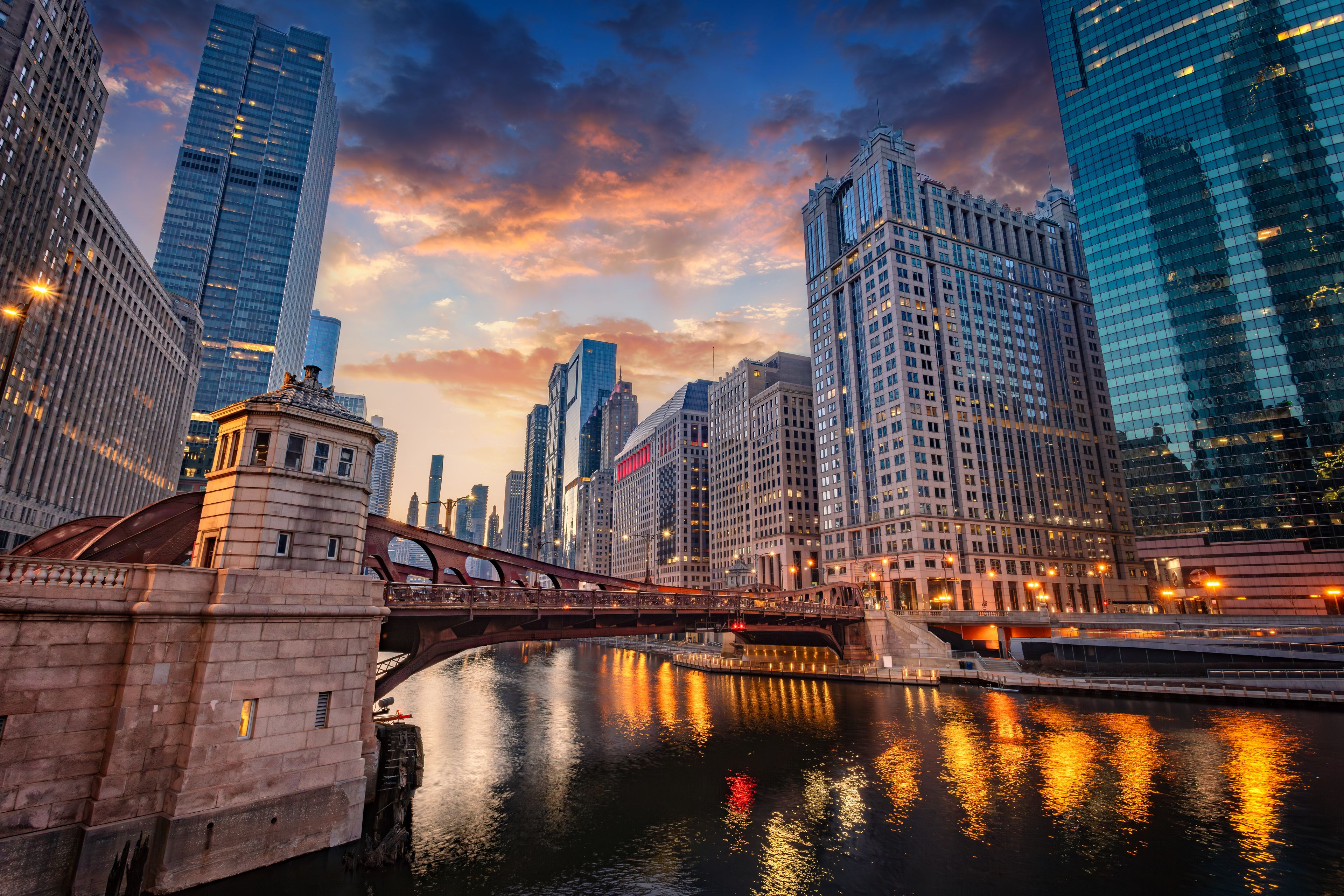 A cityscape with a river, a bridge, and modern skyscrapers reflecting in the water.