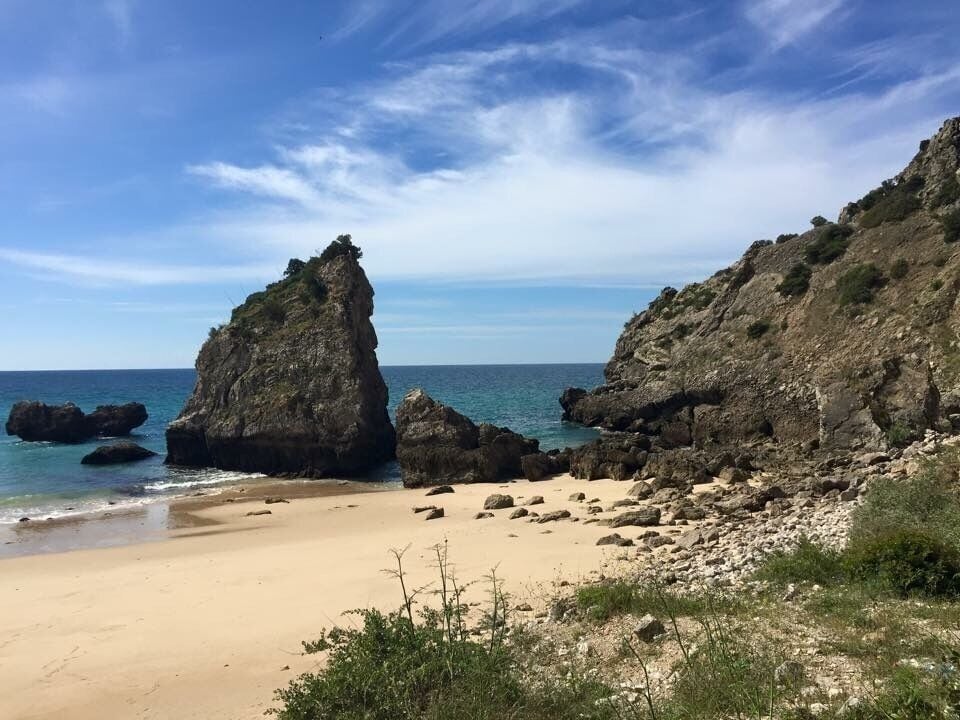 A beach with rocky cliffs and clear blue water.