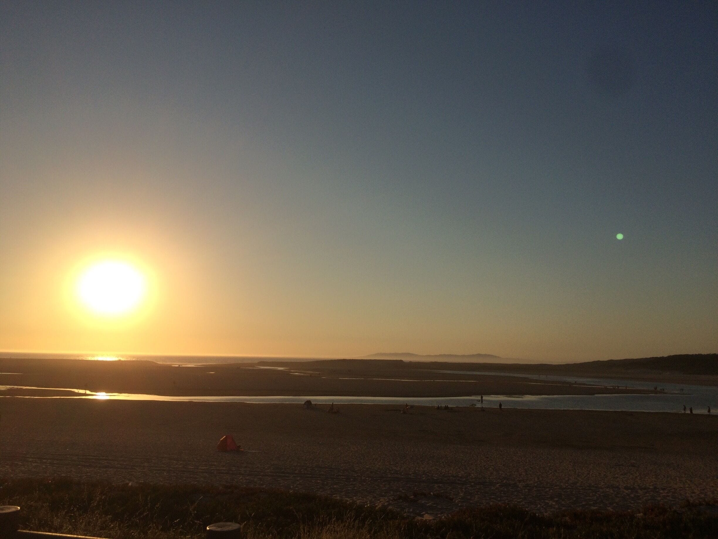 A sunset over a beach with a tent and a distant hill.