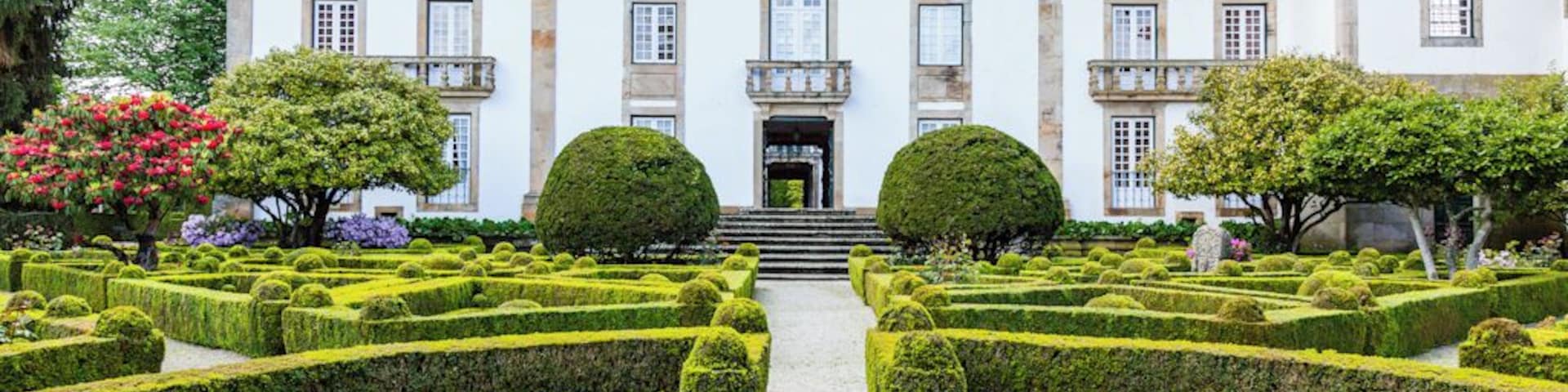 Um edifício histórico com jardins simétricos e uma fonte central.