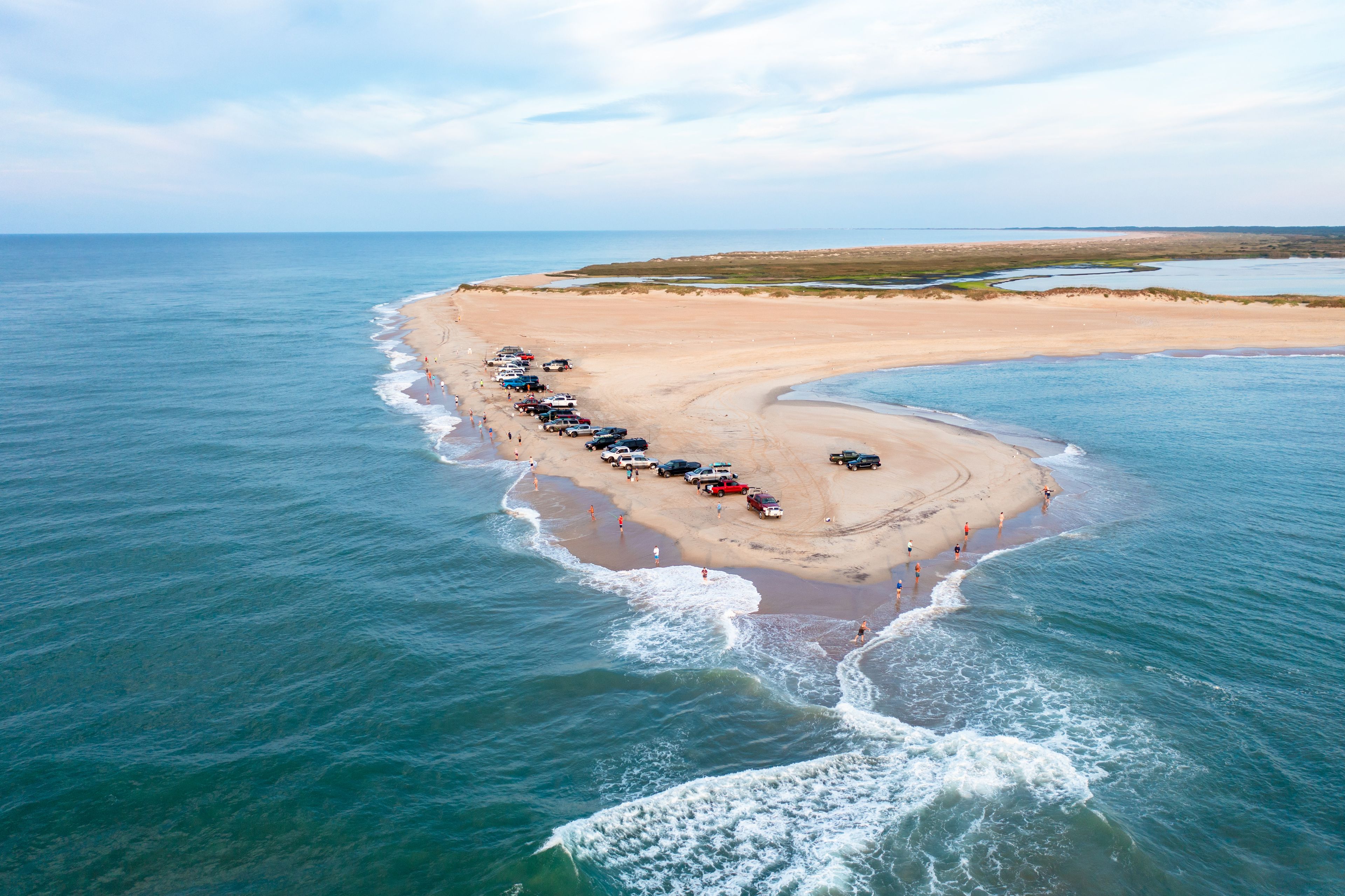 An aerial view of a beach with parked cars and people.
