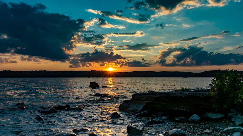 A sunset over a lake with rocks and a distant shoreline.