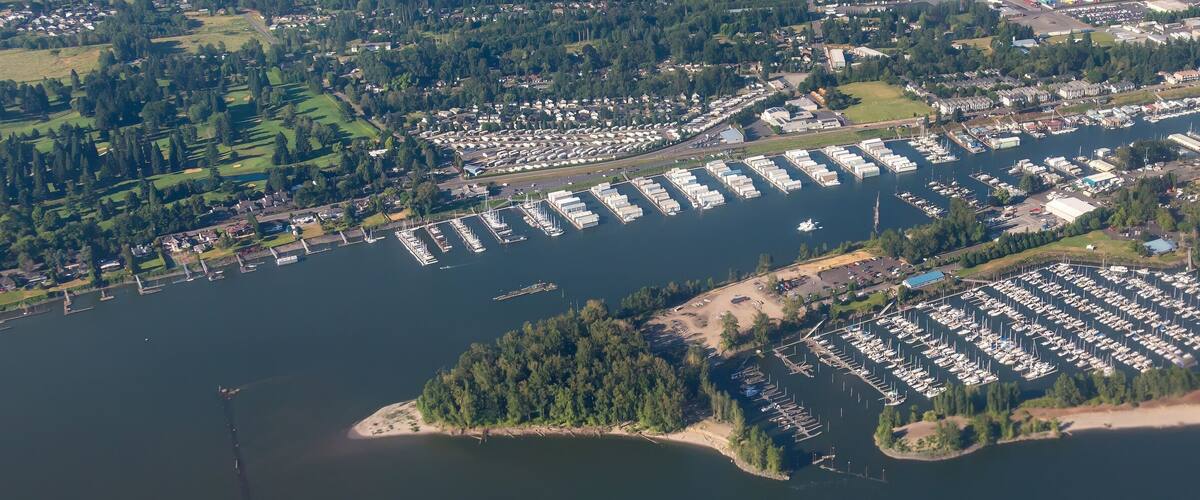 An aerial view of a marina with numerous boats docked, surrounded by residential areas and greenery.