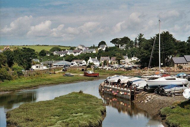 A riverside village with boats docked along the shore, surrounded by houses and greenery.