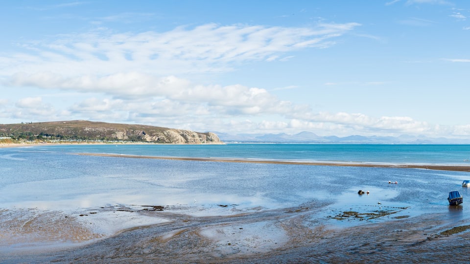 A beach with boats, calm water, and a distant mountain.
