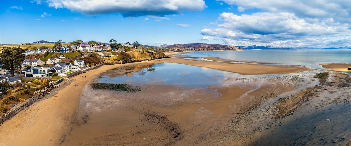 A coastal town with sandy beaches, a calm sea, and a backdrop of hills.