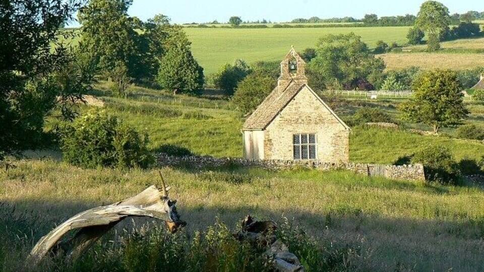 A stone house with a thatched roof surrounded by a grassy field and trees.