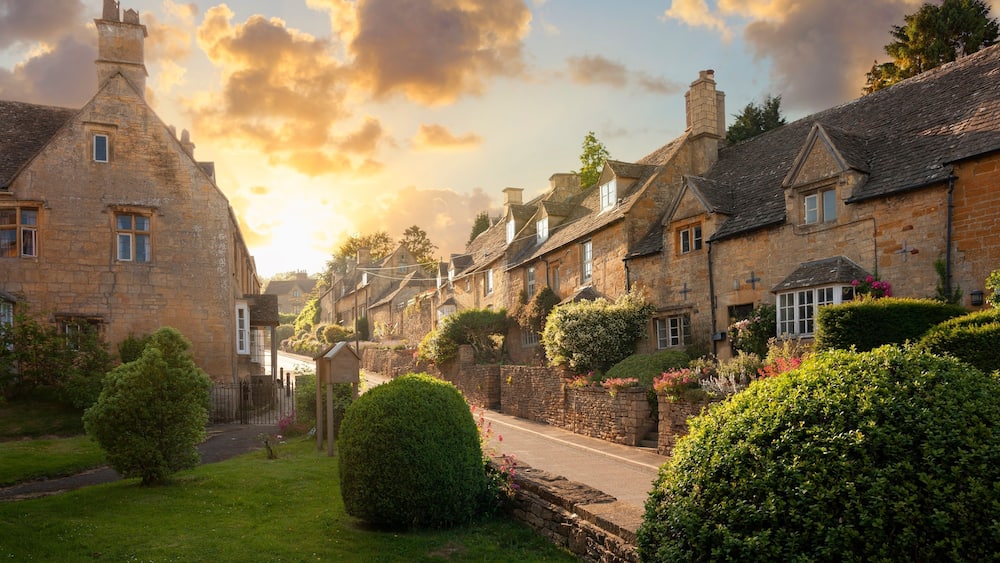 A quaint village with stone buildings, a cobblestone street, and lush greenery.