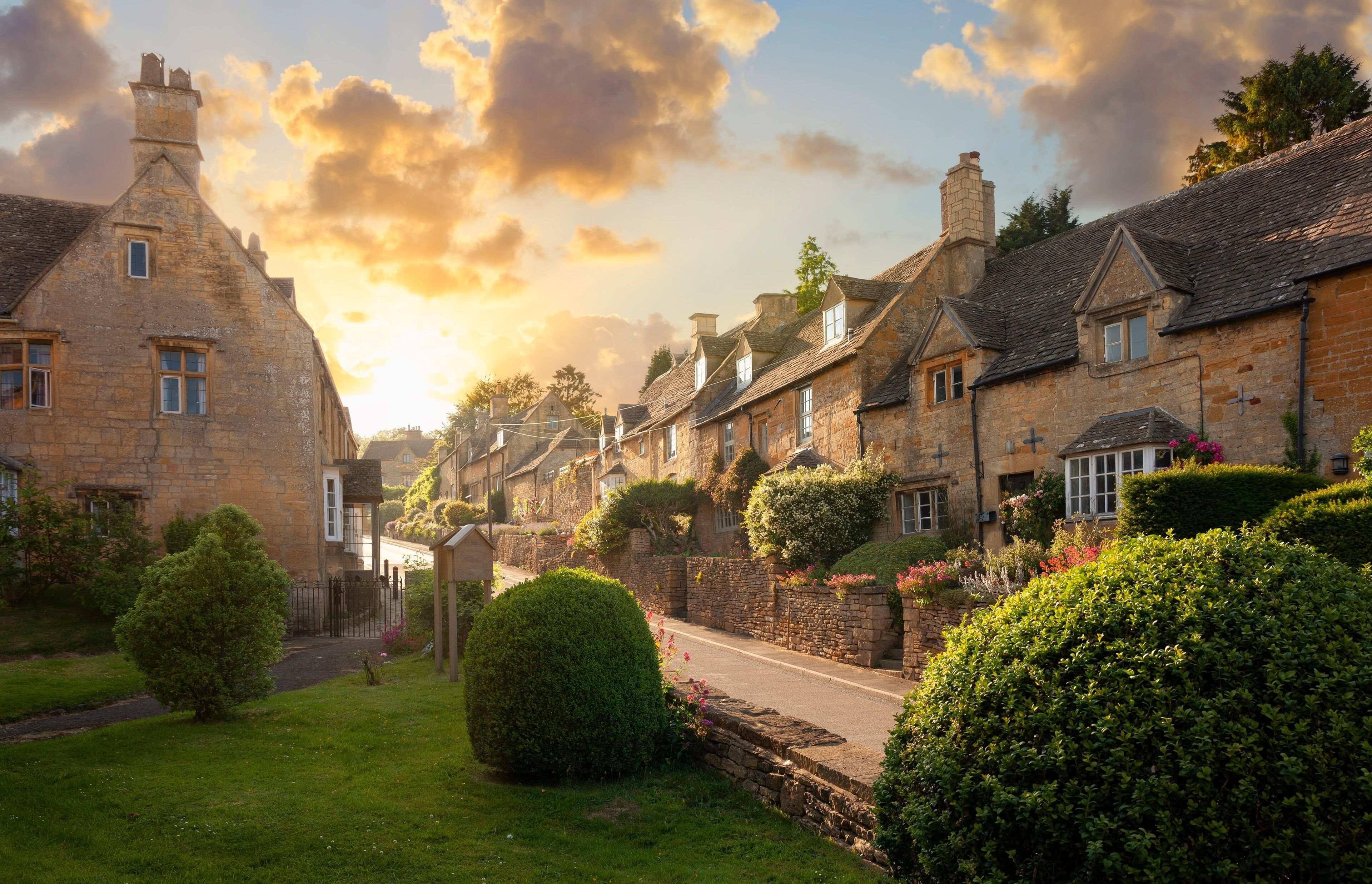 A quaint village with stone buildings, a cobblestone street, and lush greenery.
