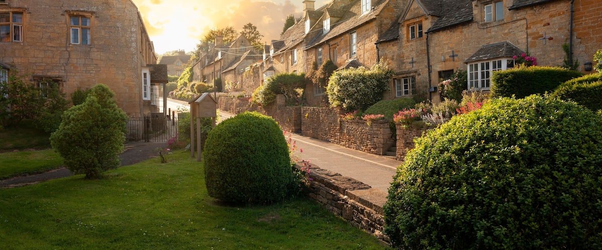 A quaint village with stone buildings, a cobblestone street, and lush greenery.