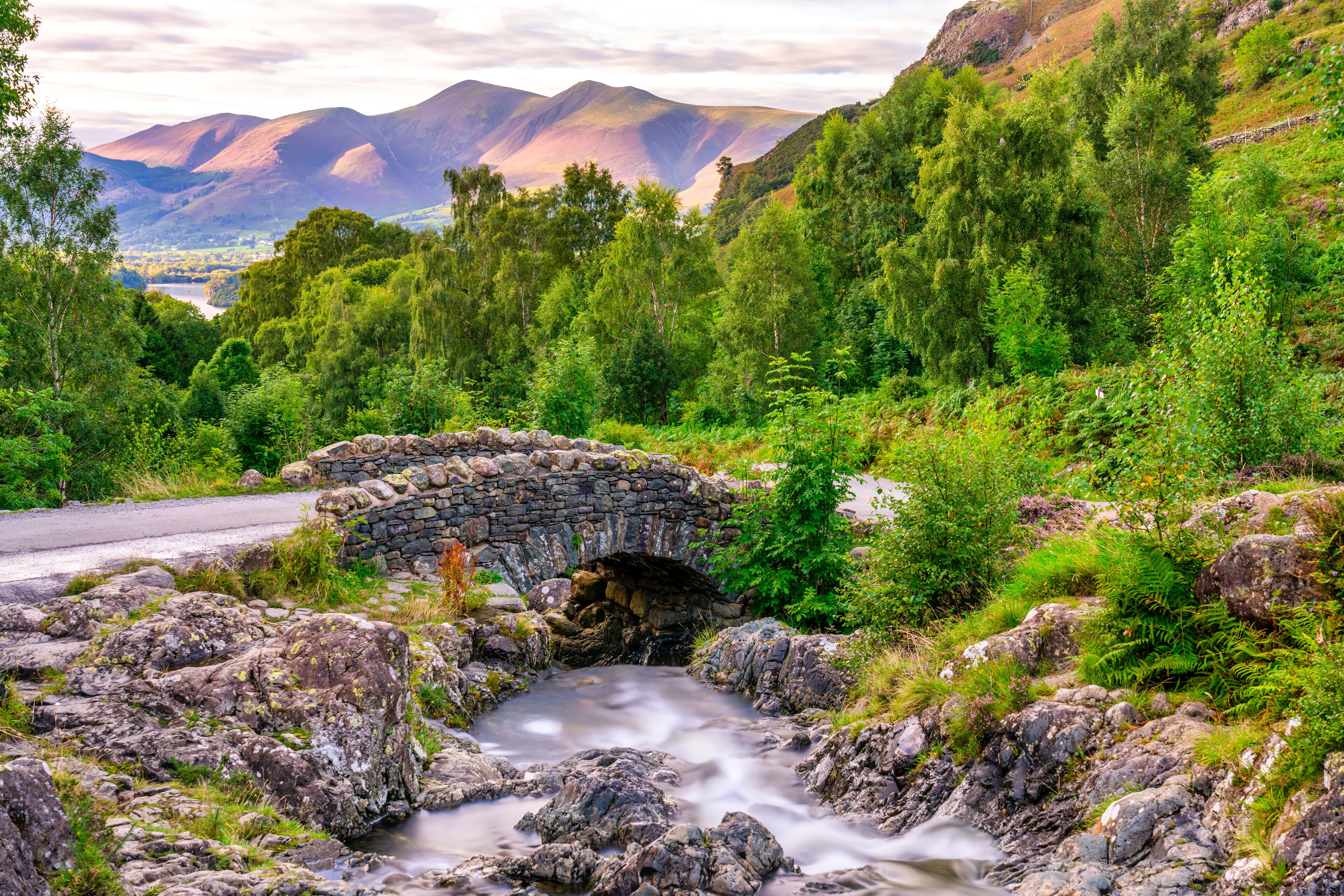 A stone bridge over a stream in a lush green valley with mountains in the background.