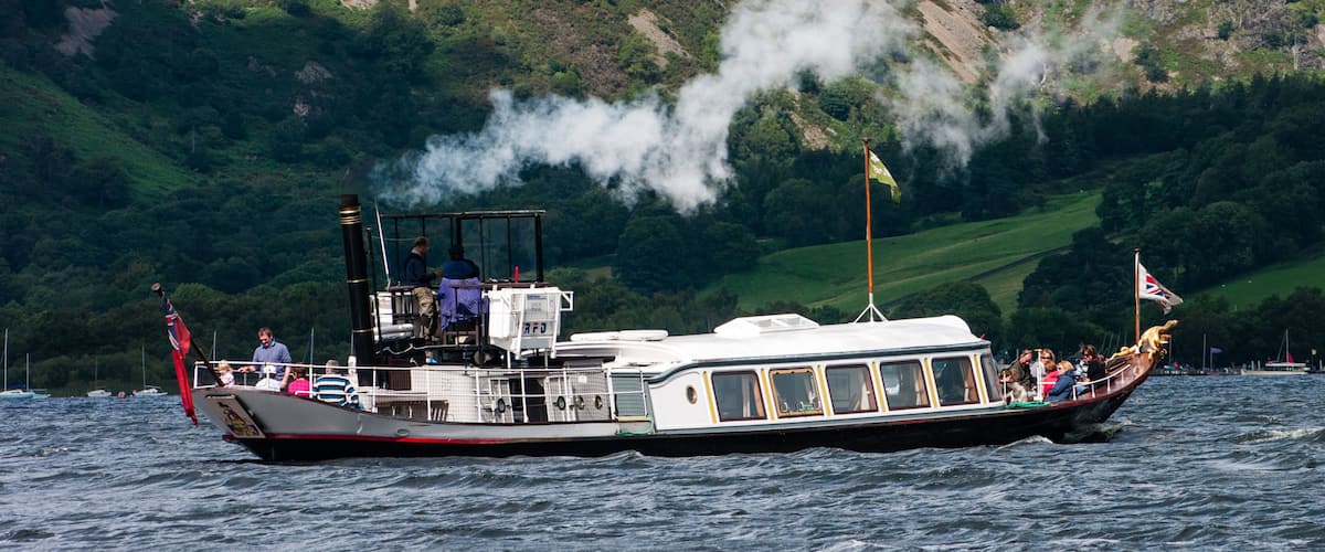 Um barco a vapor com passageiros e uma bandeira, cercado por uma paisagem montanhosa e um corpo de água.