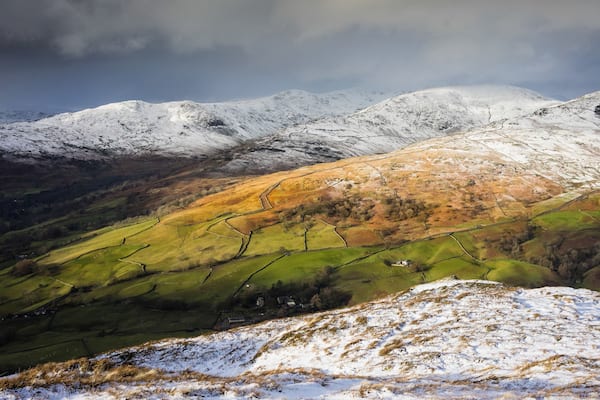 A snow-covered mountain range with green valleys and a small village.