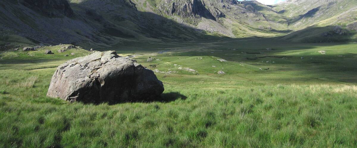 A mountainous landscape with a prominent rock in the foreground and a valley in the background.