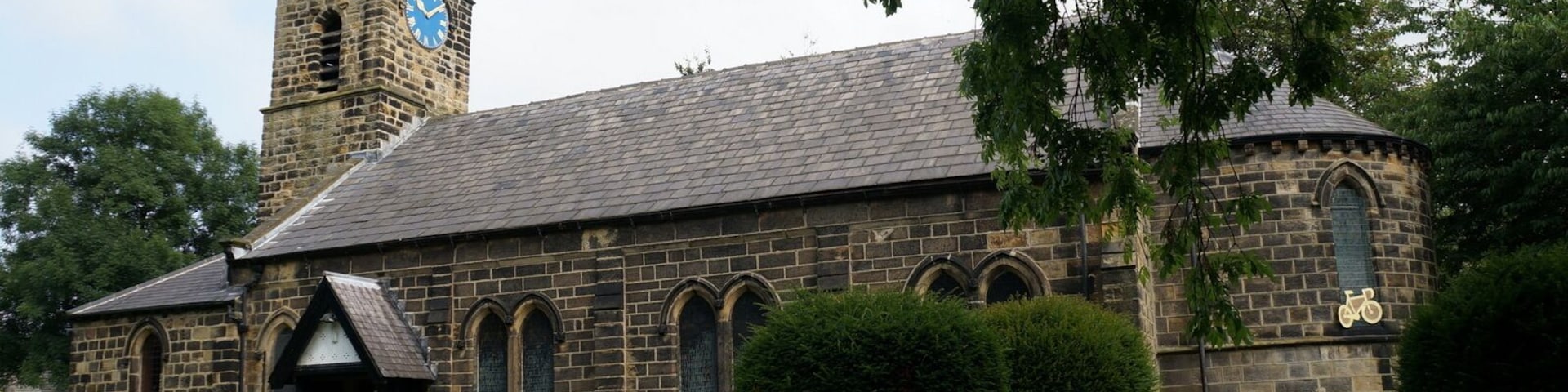 A historic church with a tall steeple and a clock, surrounded by well-maintained greenery.