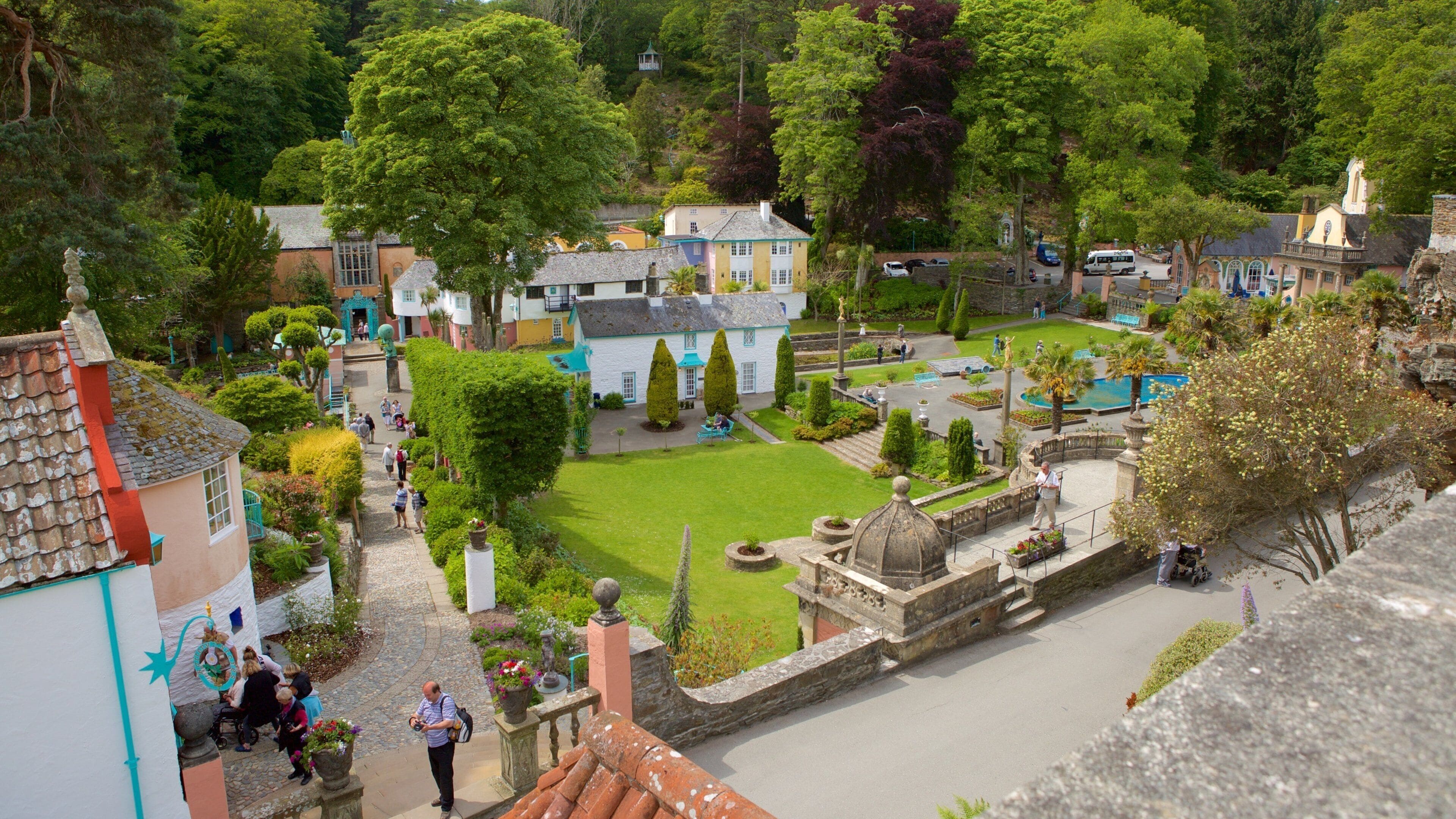 A lush garden with a central lawn, surrounded by colorful buildings and statues.