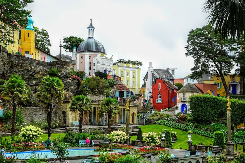 A colorful garden with a fountain, a pool, and a variety of plants and flowers.