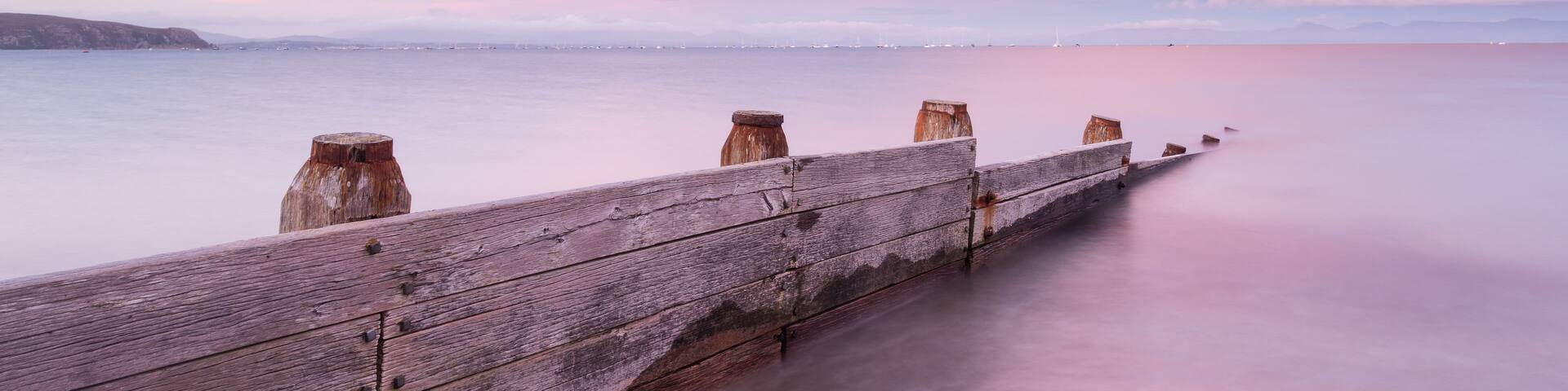 A wooden pier extending into calm waters with a pink and purple sky.