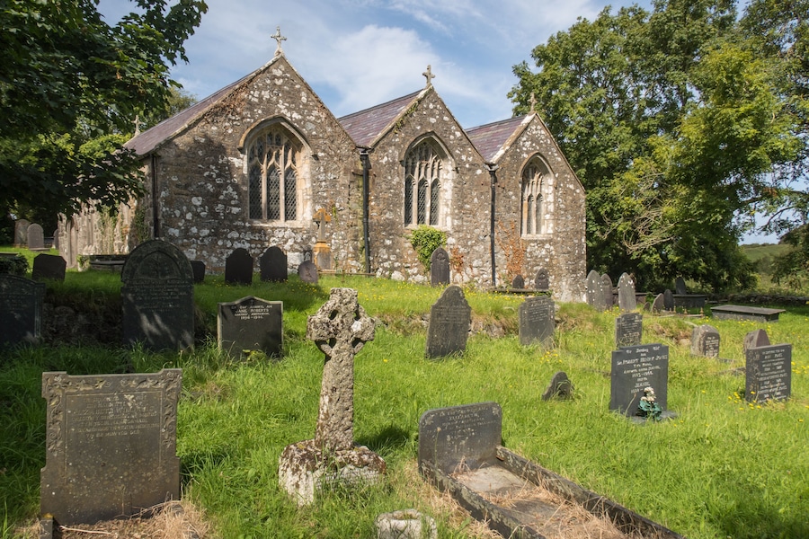 A historic church with stone walls and pointed arches, surrounded by a cemetery with headstones and crosses.