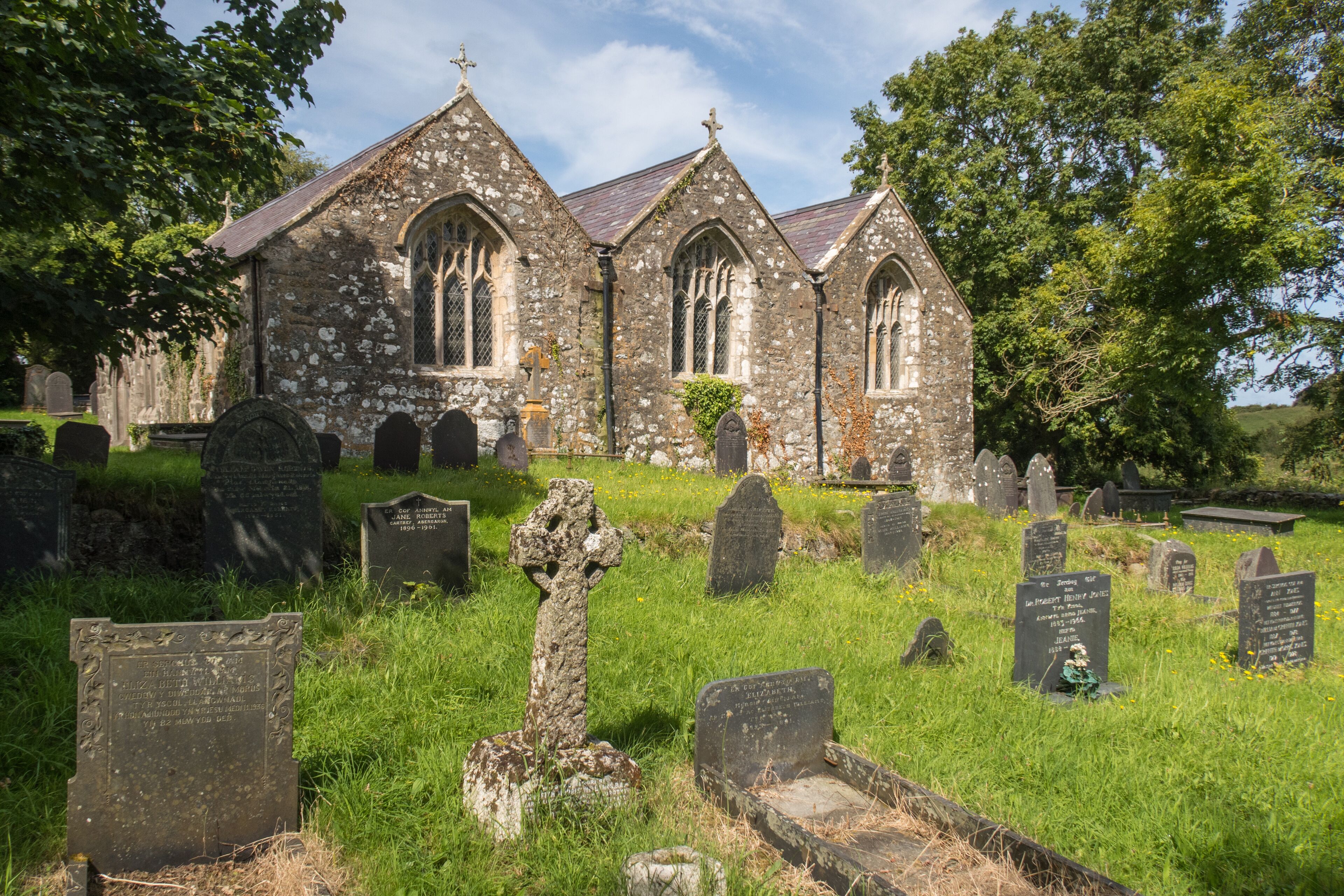 A historic church with stone walls and pointed arches, surrounded by a cemetery with headstones and crosses.