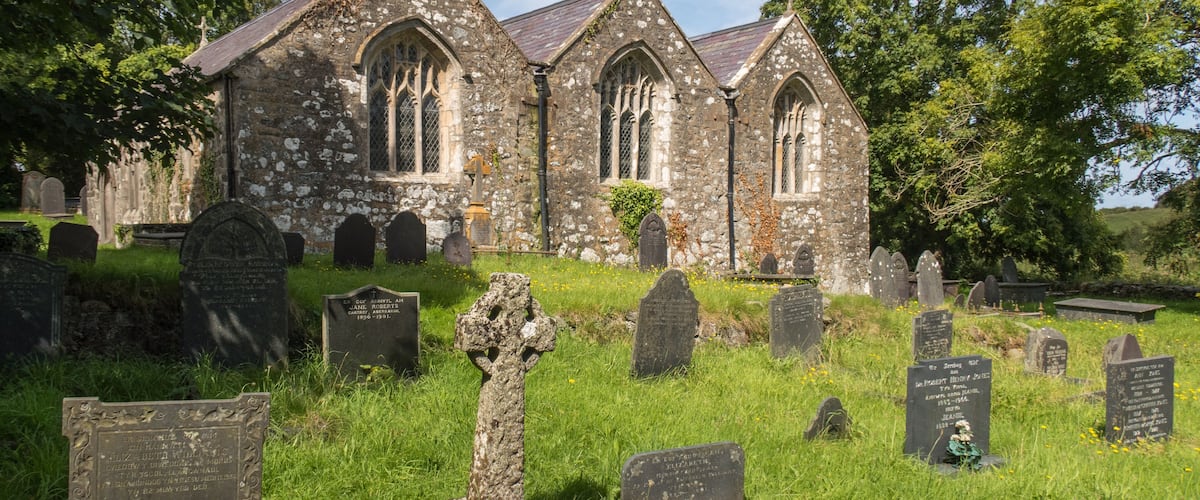 A historic church with stone walls and pointed arches, surrounded by a cemetery with headstones and crosses.