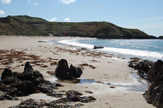 Ein Strand mit Felsen und einer grasbewachsenen Hügelkette im Hintergrund.