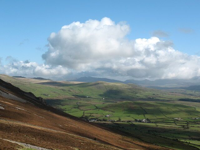 A valley with rolling hills, a large cloud, and scattered houses.