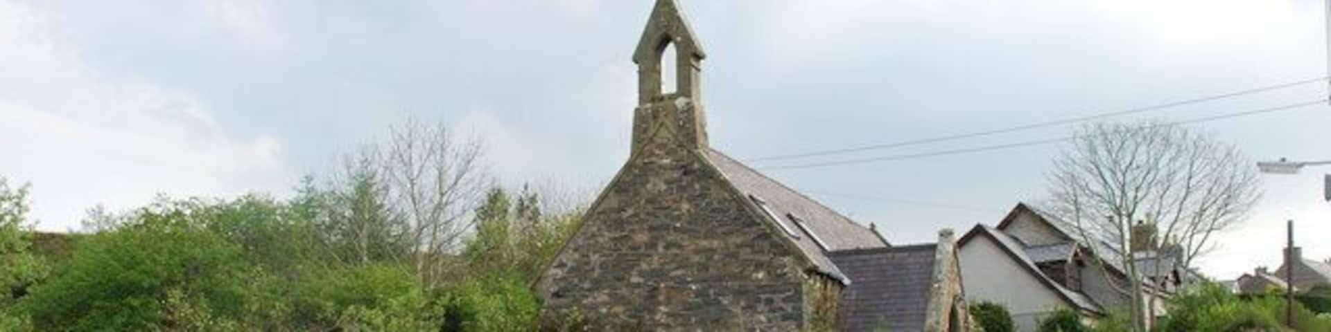 A stone church with a steeple, surrounded by greenery and houses.