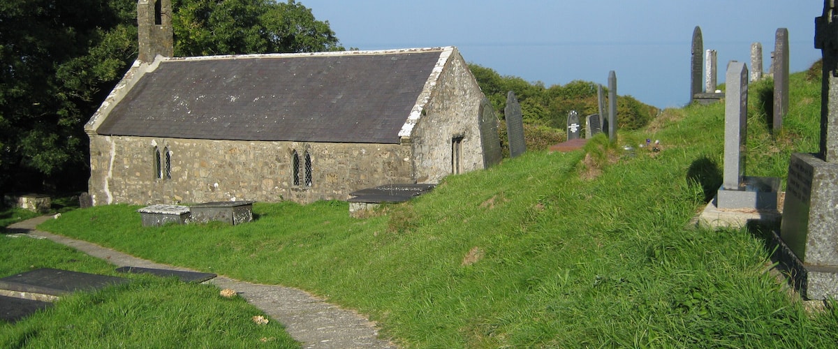 A stone church with a grassy path leading to it, surrounded by headstones.