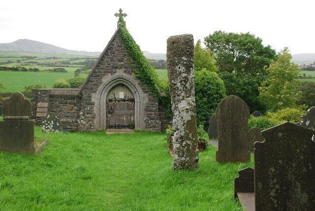 A small stone church with a cross on top, surrounded by a cemetery with headstones.