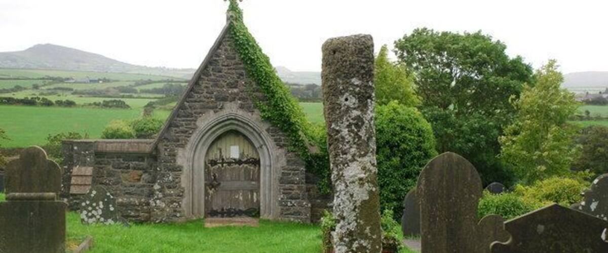 A small stone church with a cross on top, surrounded by a cemetery with headstones.