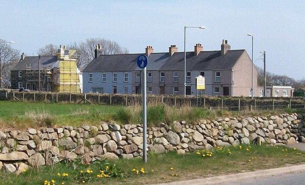 A residential area with houses, a stone wall, and a blue sign indicating a bicycle path.