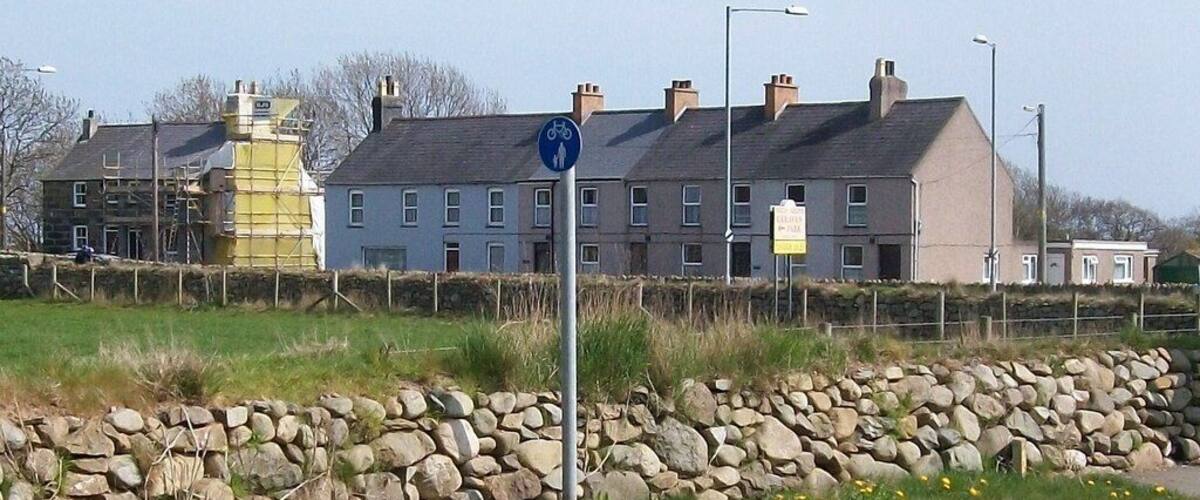 A residential area with houses, a stone wall, and a blue sign indicating a bicycle path.