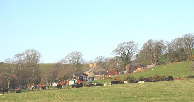 A rural landscape with a green field, sheep, and farm buildings.