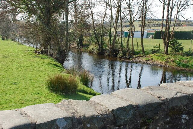 A calm river with a stone wall in the foreground and trees lining the banks.