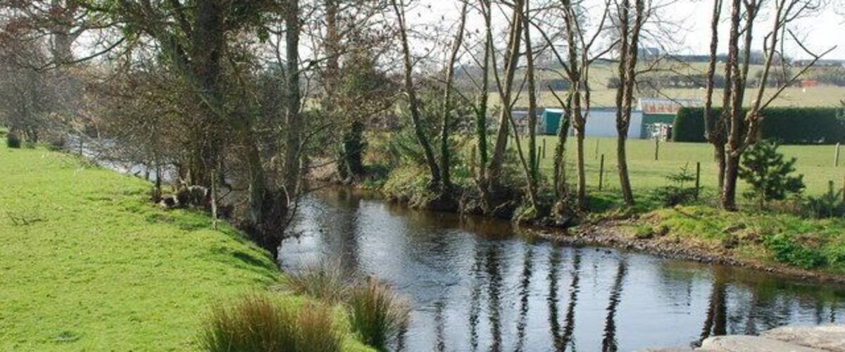 A calm river with a stone wall in the foreground and trees lining the banks.