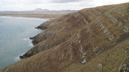 Looking across Trwyn Carreg-y-tir From Trwyn y Fulfran. Coastal erosion has exposed the rock strata which must have helped the lead mining activity around here. A trail of mine waste is visible on the lower right.