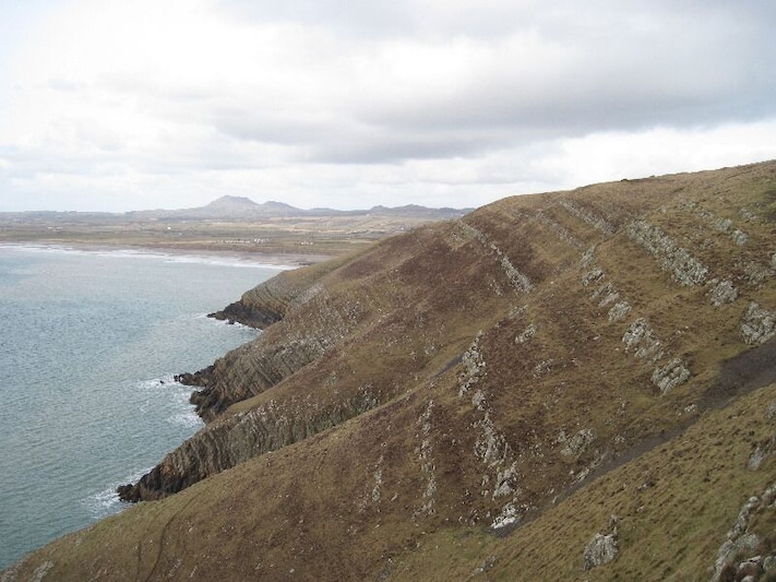 Looking across Trwyn Carreg-y-tir From Trwyn y Fulfran. Coastal erosion has exposed the rock strata which must have helped the lead mining activity around here. A trail of mine waste is visible on the lower right.