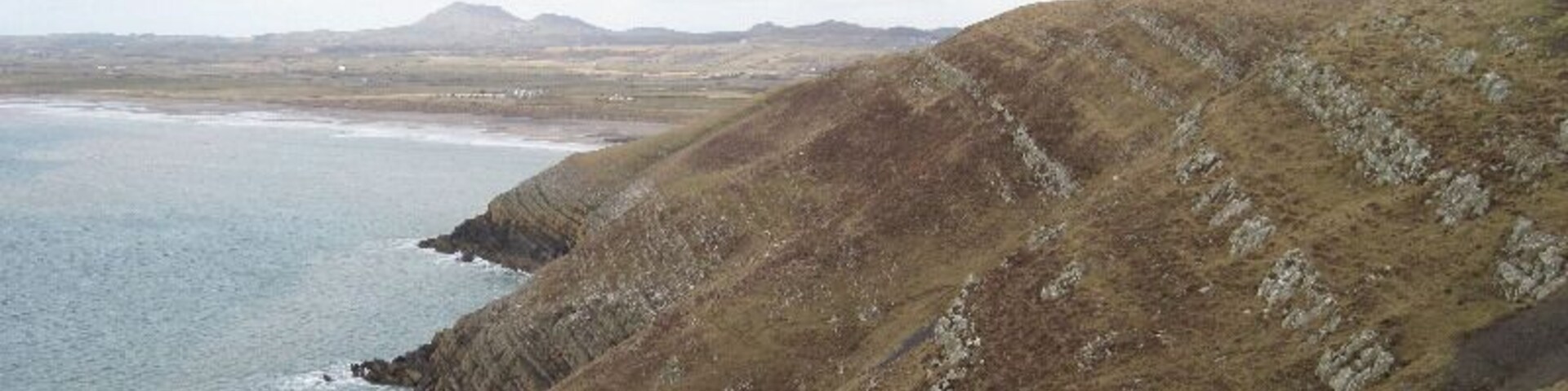 Looking across Trwyn Carreg-y-tir From Trwyn y Fulfran. Coastal erosion has exposed the rock strata which must have helped the lead mining activity around here. A trail of mine waste is visible on the lower right.