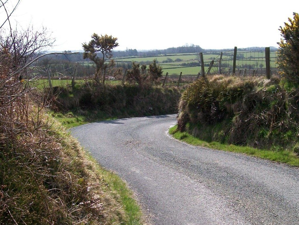 Uma estrada de cascalho estreita serpenteando por uma paisagem rural com campos e cercas.