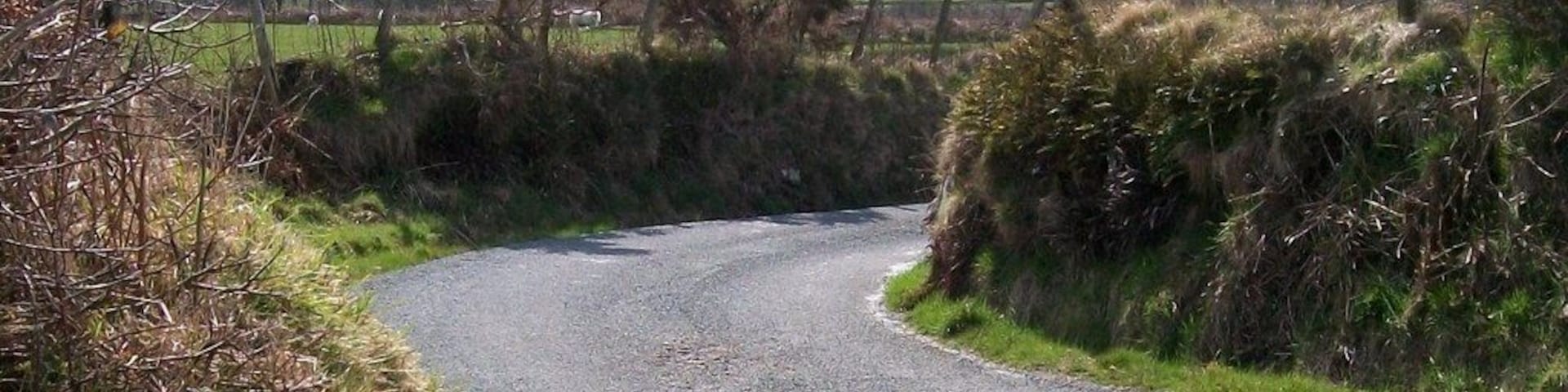 Uma estrada de cascalho estreita serpenteando por uma paisagem rural com campos e cercas.