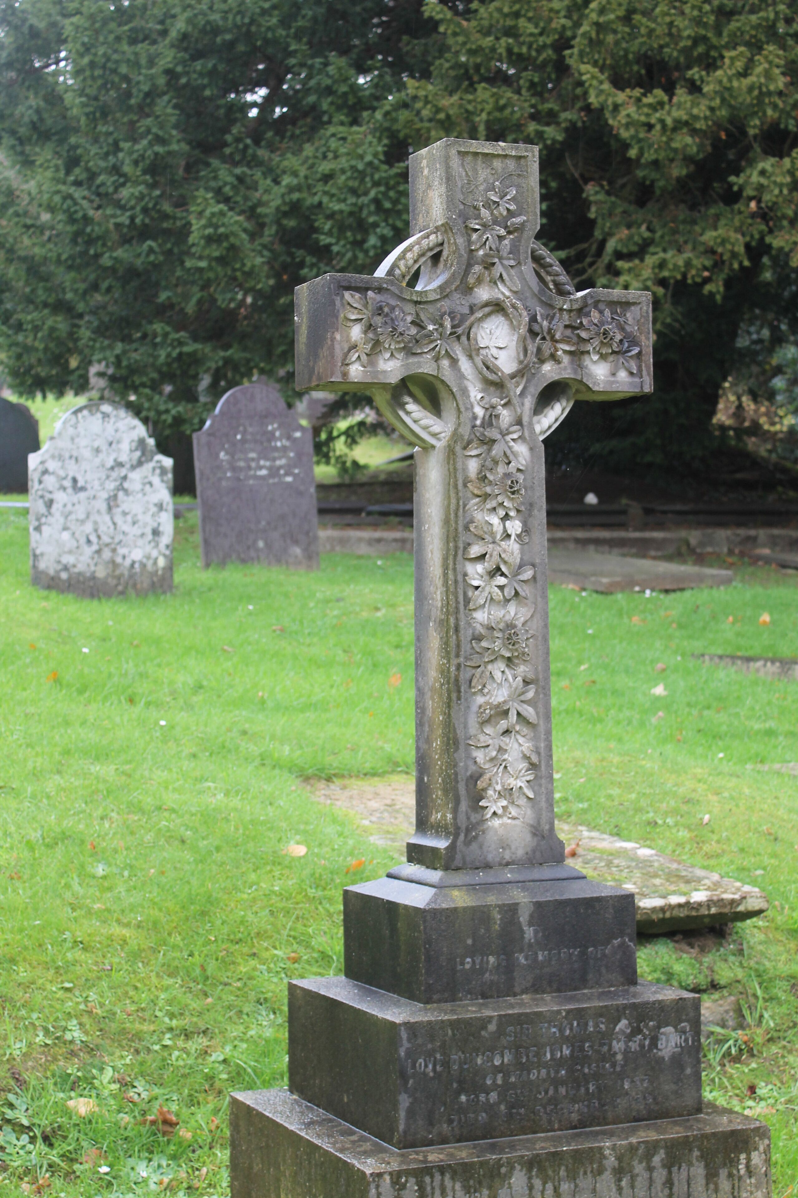 A stone cross with floral carvings and inscriptions in a cemetery.