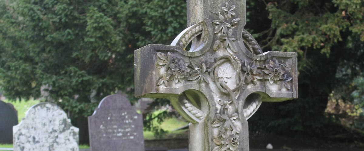 A stone cross with floral carvings and inscriptions in a cemetery.