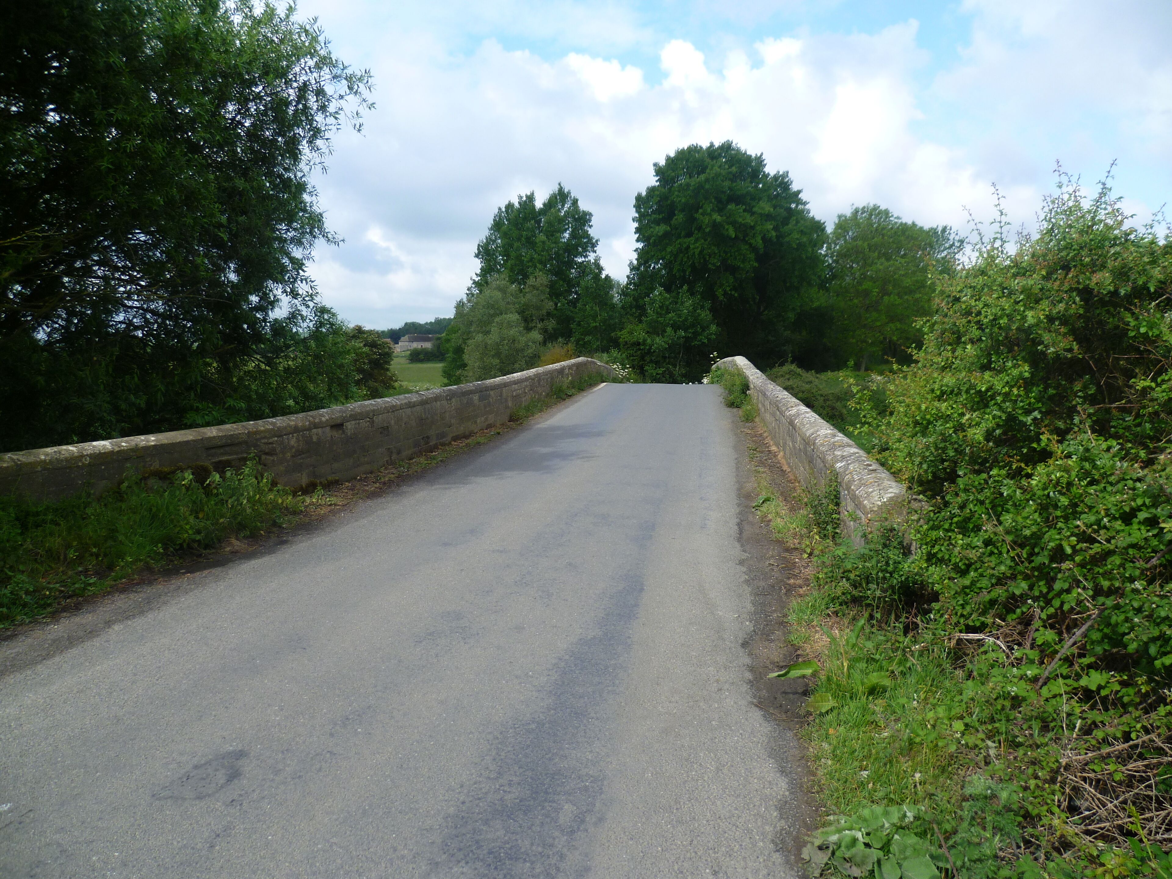 A narrow rural road flanked by stone walls and lush greenery.