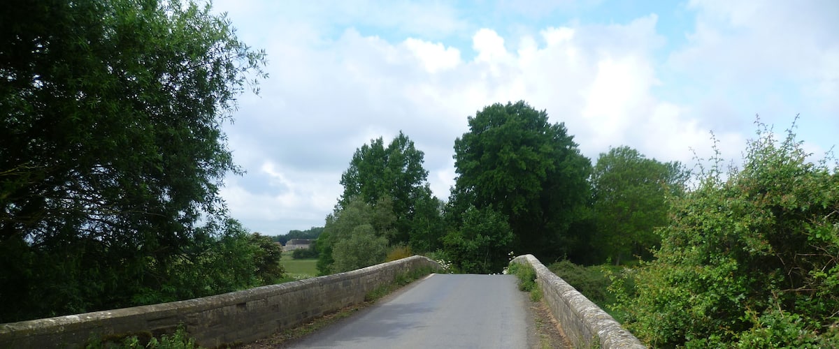 A narrow rural road flanked by stone walls and lush greenery.