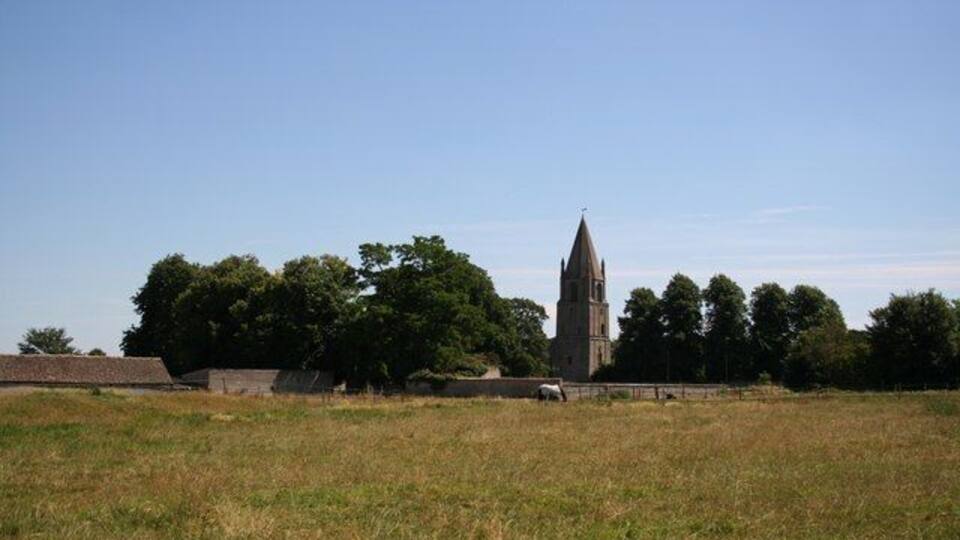 A church with a tall spire, surrounded by trees and open fields.
