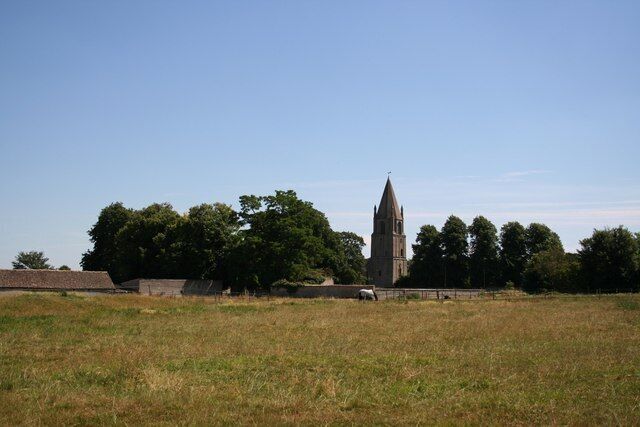 A church with a tall spire, surrounded by trees and open fields.